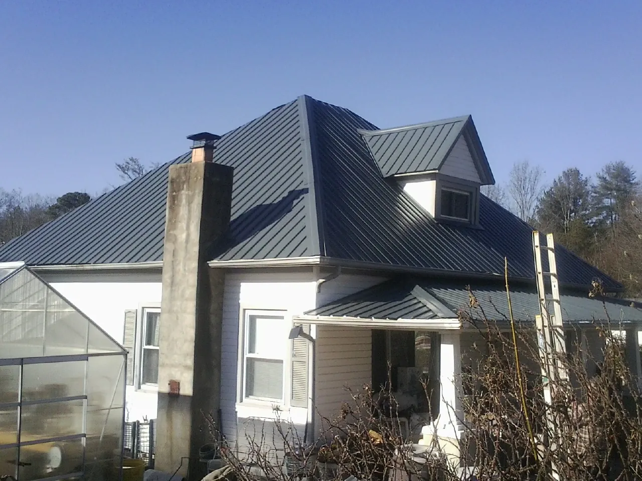 Dark blue standing seam metal roof on a white farmhouse with dormer — Slate & Tile Roof Repair by Roofing Brothers in Belle Mead
