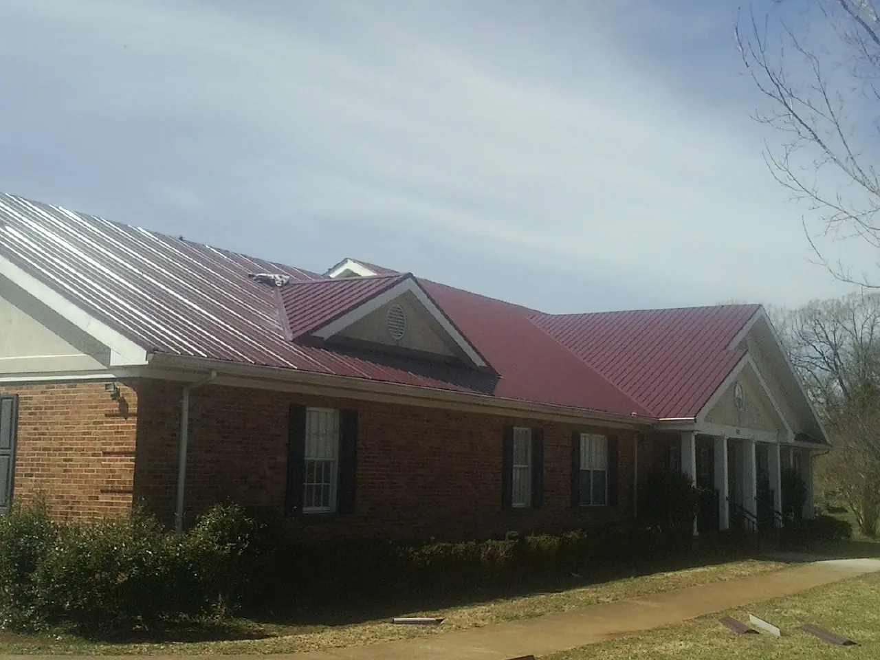Red metal roof with gabled entries on a long brick building, from a Hail Damage Roof Repair job in Belle Mead