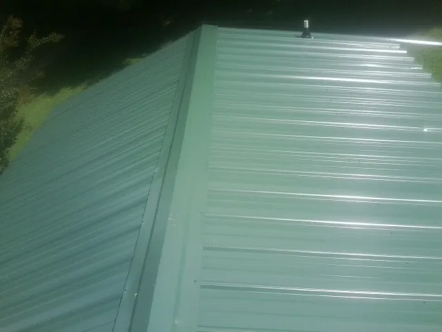 New green metal panels meeting at the ridge of a roof — Flat Roof Repair work by our crew in Belle Mead
