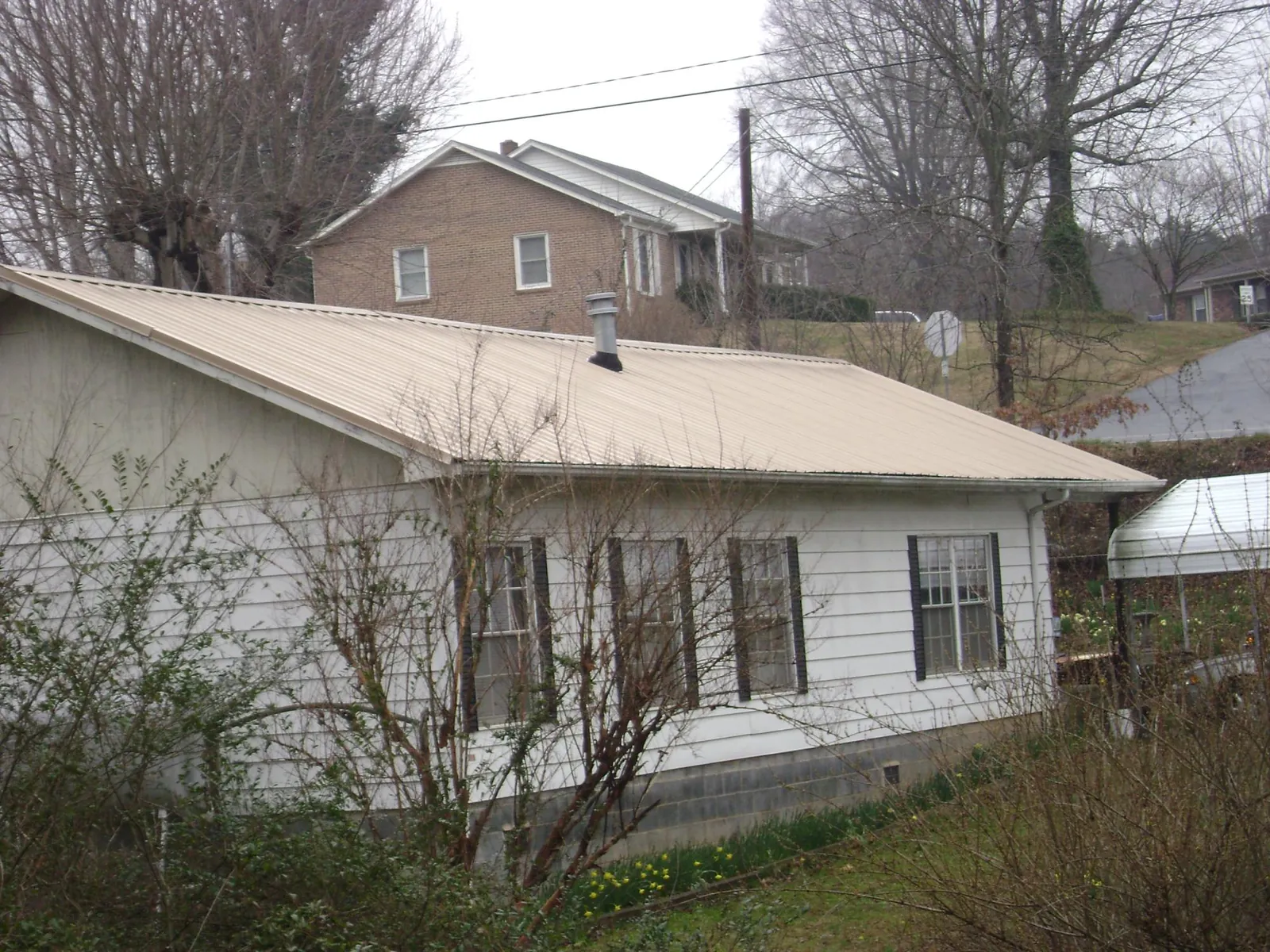 Tan metal roof on a white sided house set into a hillside — Commercial Roofing by Roofing Brothers in Belle Mead